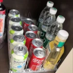 Drink pusher system maintaining alignment of soda cans inside display fridge. 21. Shelf pushers installed in a home refrigerator for bottled drinks organization.